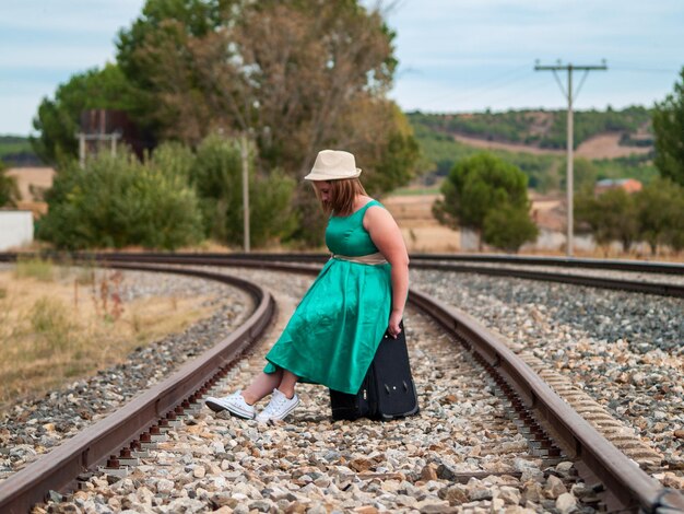 Full length of woman sitting on luggage at railroad track