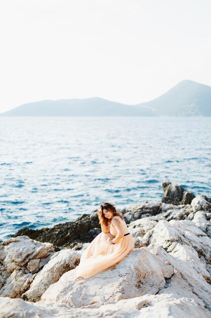 Foto lunghezza completa di una donna seduta su una roccia contro il mare