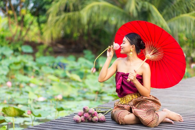 Foto lunghezza completa di donna che puzza di fiore mentre tiene un ombrello seduto sul molo