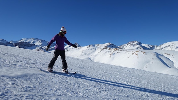 Lunghezza completa di una donna che fa snowboard contro un cielo blu limpido