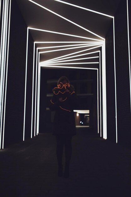 Foto lunghezza completa della donna in piedi contro le luci illuminate sul muro