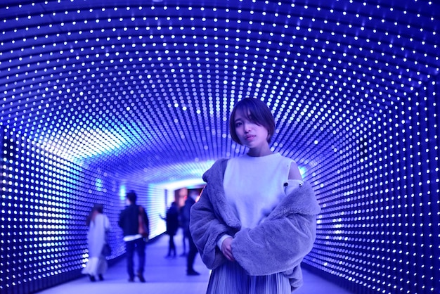 Foto lunghezza completa di una donna in piedi contro un muro illuminato