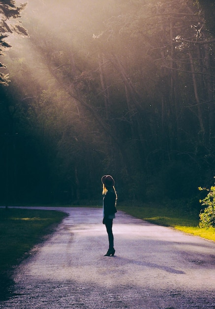 Foto lunghezza completa di una donna in piedi sulla strada in mezzo agli alberi