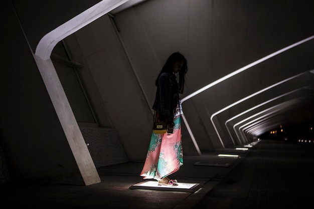 Foto lunghezza completa di una donna in piedi sulla lampada di strada di notte