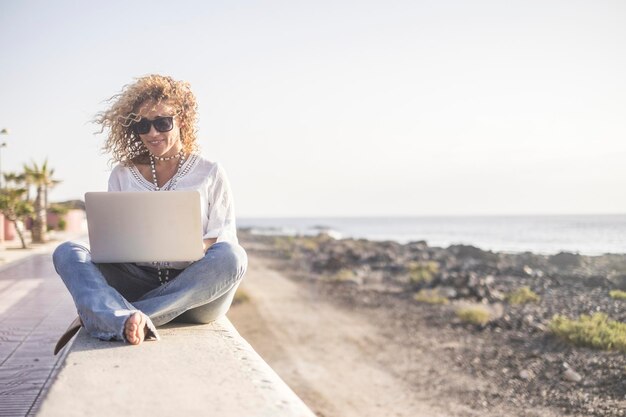 Photo full length of woman using laptop while sitting at beach against sky