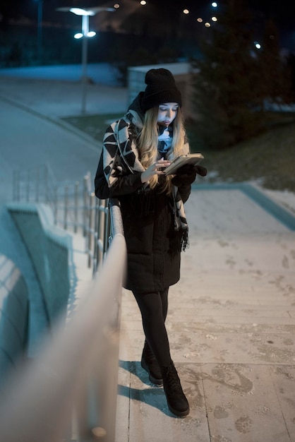 Full length of woman using smart phone while standing by railing at night