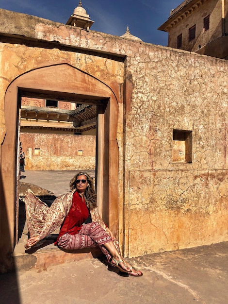 Foto lunghezza completa di una donna che indossa un vestito seduta alla porta di un edificio storico