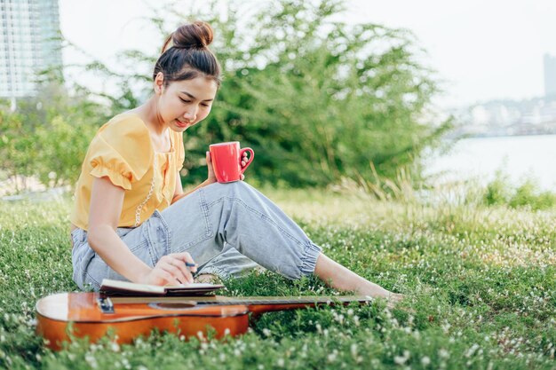 Full length of woman writing on book while having drink at park