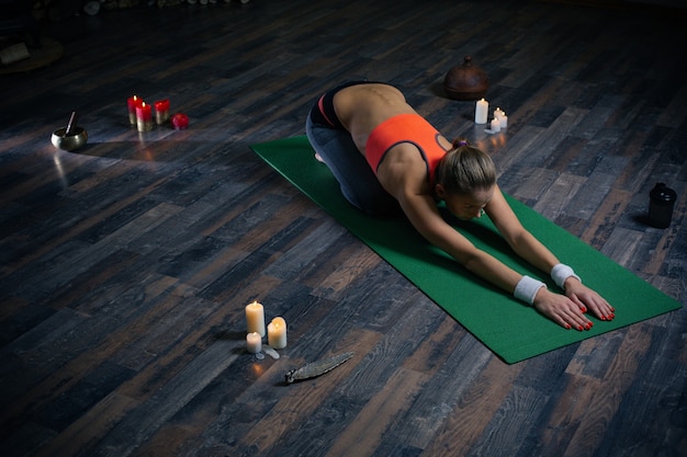 Полная длина тренировки йоги и молодая женщина, склоняющаяся к земле во время практики асаны на коврике для йоги со свечами вокруг нее