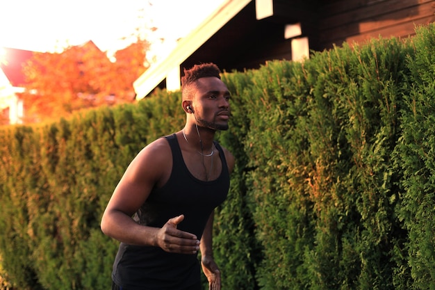 日没や日の出で、屋外で運動しながらジョギングをしているスポーツウェアの若いアフリカ人の全身。ランナー。