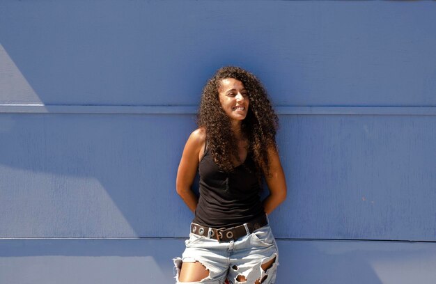 Photo full length of young arabic woman standing against blue wall in summer