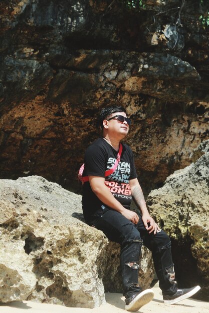 Photo full length of young man sitting on rock