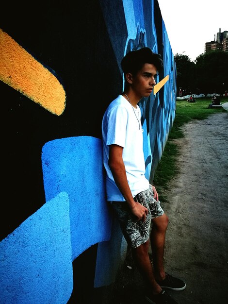 Photo full length of young man standing by graffiti wall