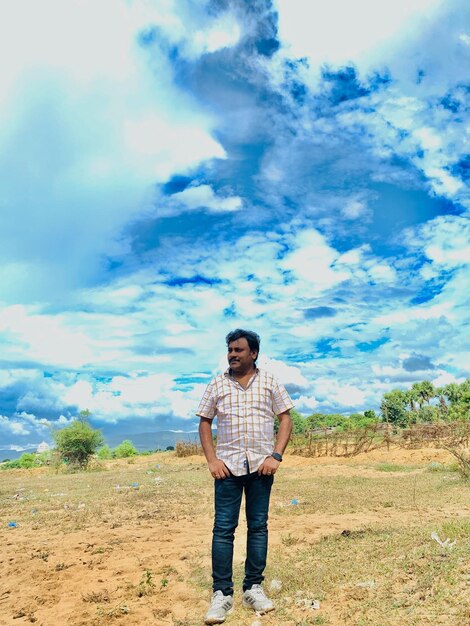 Full length of young man standing on field against sky