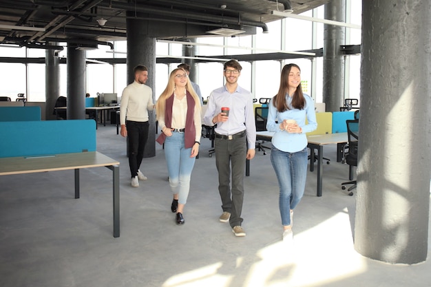 Full length of young people in smart casual wear discussing business and smiling while walking through the office.