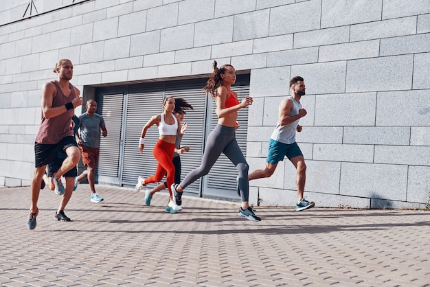 Full length of young people in sports clothing jogging while exercising on the sidewalk outdoors