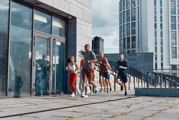 Full length of young people in sports clothing jogging while exercising on the sidewalk outdoors