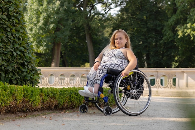 Photo full length young pretty woman with short stature on wheelchair looking at camera in public park at