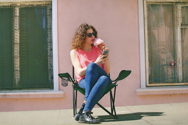 Full length of young woman eating ice cream while sitting in city during sunny day