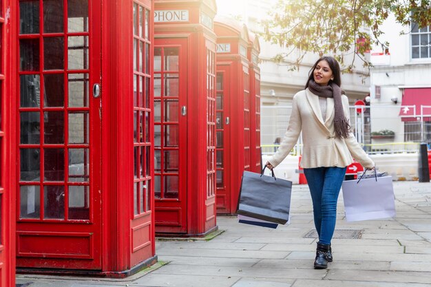 Full length of young woman holding shopping bags while walking on footpath in city