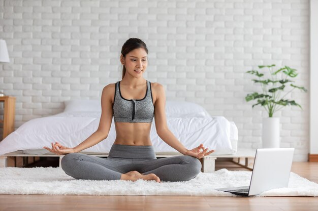 full length of young woman looking at laptop while meditating at home