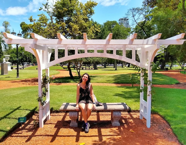 Foto lunghezza completa di una giovane donna sul sedile al parco