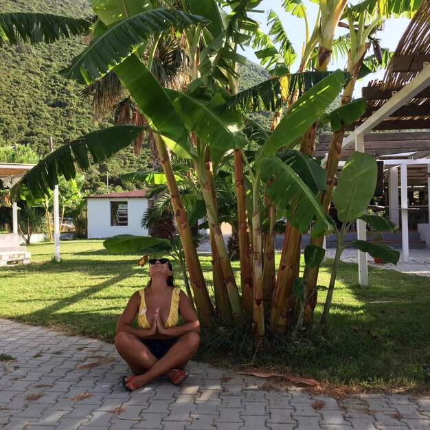 Foto lunghezza piena di giovane donna seduta contro gli alberi