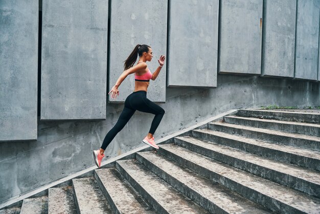 屋外の階段で運動しながらジョギングスポーツ服の若い女性の全長