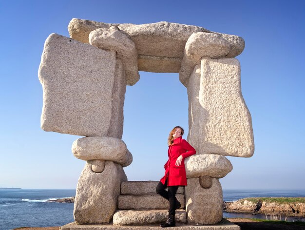 Foto lunghezza completa di una giovane donna in piedi dalla formazione rocciosa contro il mare