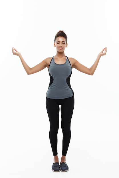 Photo full length of young woman with eyes closed doing yoga while standing against white background