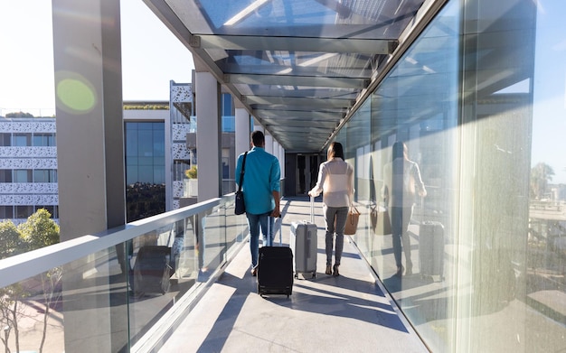 Full lengthy rear view of young biracial male and female colleagues with luggage walking at corridor