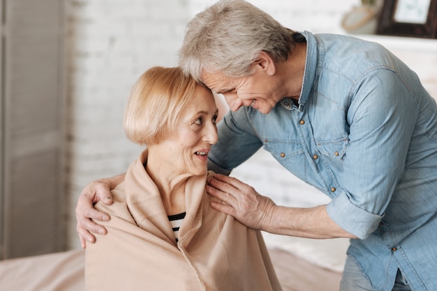 Pieno d'amore. persone anziane adorabili e affascinanti che ridono insieme mentre l'uomo soddisfa i favori delle signore e le porta una coperta