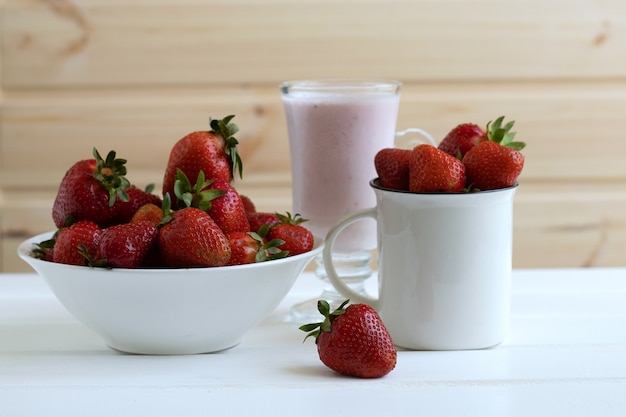 a full mug and plate of strawberries and a glass of milkshake on a white wooden wall