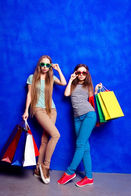 Full photo of two trendy women in glasses holding shopping bags