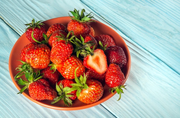 The full plate of strawberries and a cut piece on a blue table. Strawberry Diet Idea