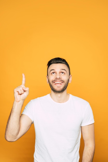 Full of pleasant emotions boy in white basic T-shirt is pointing on something what he really enjoys and recommend