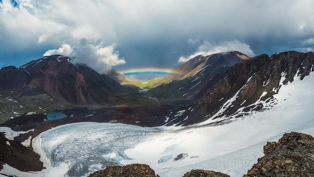 Arcobaleno completo su una valle di montagna glaciale. paesaggio alpino atmosferico con montagne innevate con arcobaleno in caso di pioggia e tempo soleggiato.