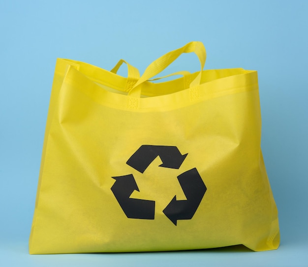 Концепция сокращения количества пластиковых отходов в полностью многоразовом желтом вискозном пакете на синем фоне