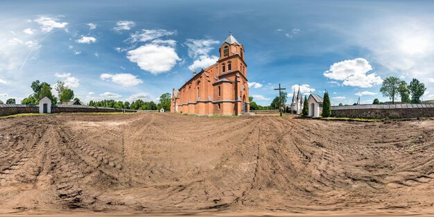 Full seamless hdri panorama 360 degrees angle view red brick\
facade of church in decorative medieval neo gothic style\
architecture in small village in equirectangular spherical\
projection vr content