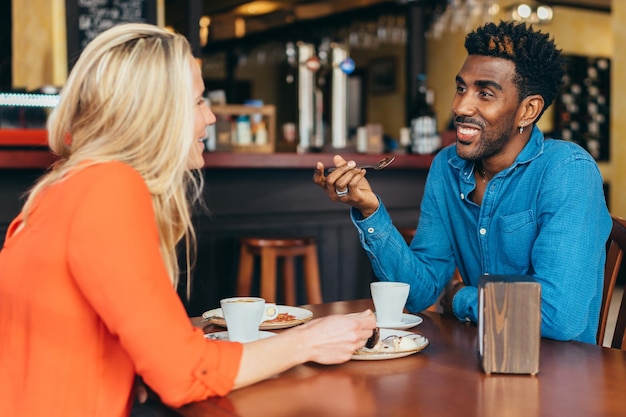 Full shot of a black man drinking coffee and eating chocolate with a Caucasian woman in a restaurant
