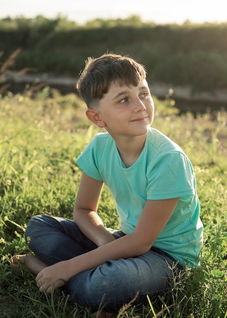 Foto ragazzo pieno del colpo che si siede sull'erba