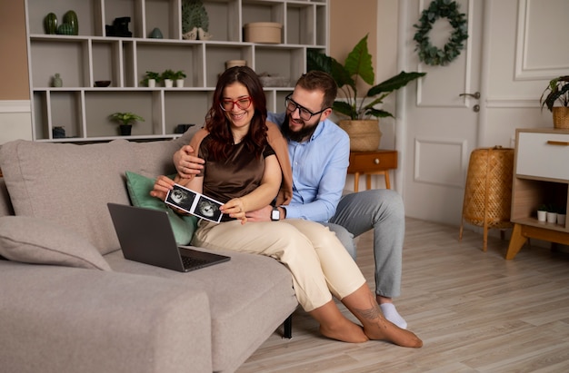 Full shot couple announcing pregnancy with laptop