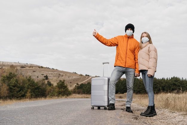 Photo full shot couple hitchhiking with masks