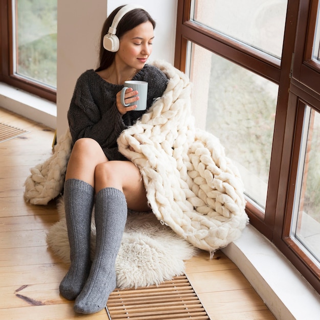 Full shot cozy woman with blanket and mug