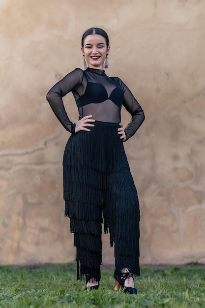 Full shot of a fulllength portrait of a smiling flamenco\
ballerina with black fringed pants