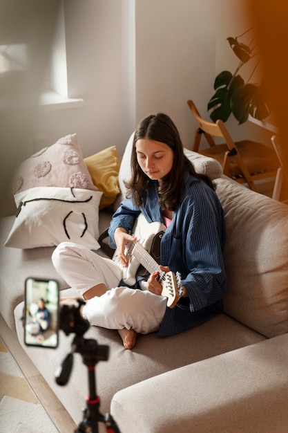 Foto ragazza del colpo pieno che suona la chitarra a casa