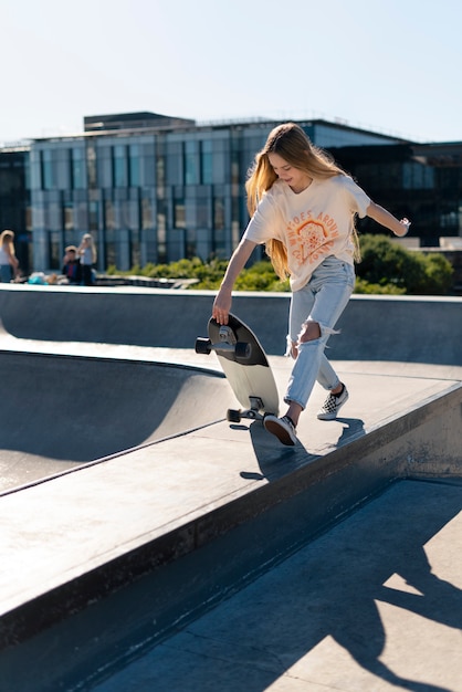 写真 屋外でスケート ボードを持つフル ショットの女の子