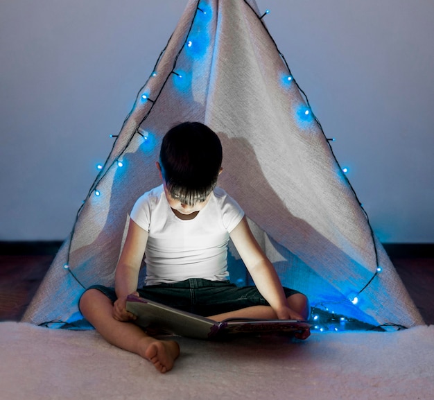 Full shot kid reading in tent