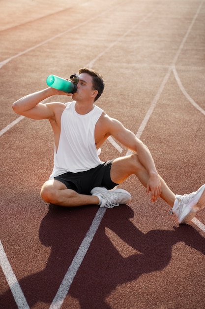 ランニングトラックでフルショットの男が水を飲む