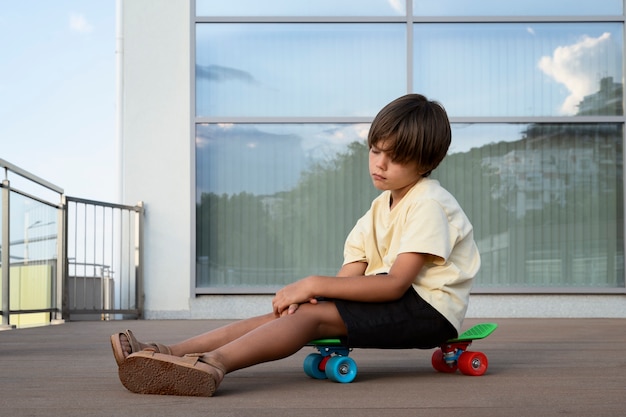 Photo full shot sad boy sitting on skateboard